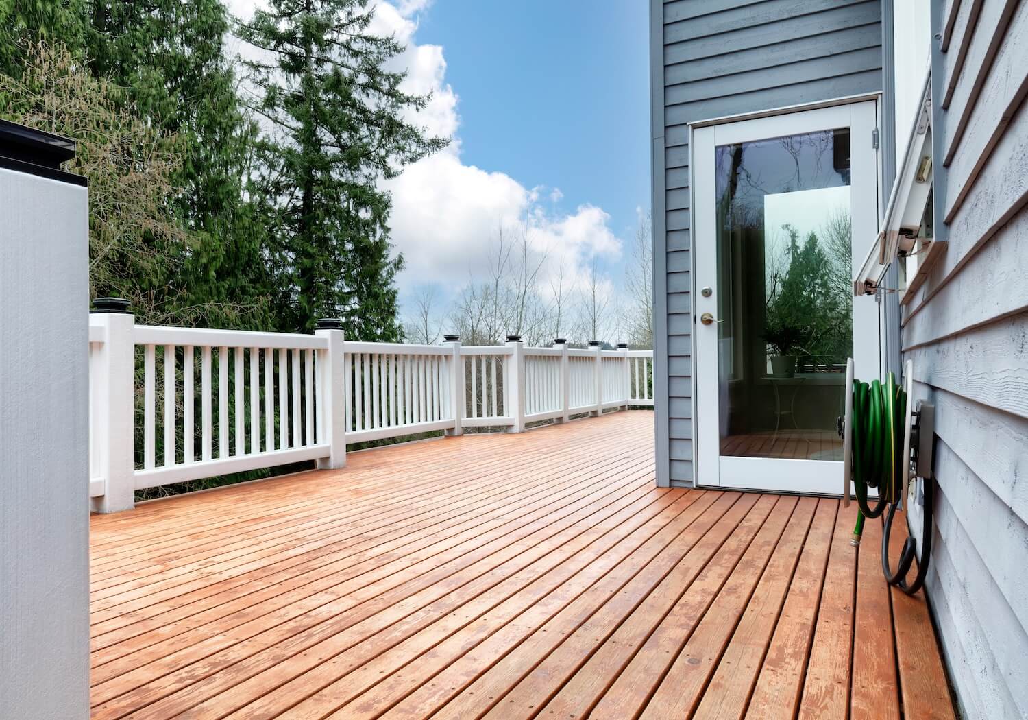 Stained wood deck with crisp white painted railings on a gray sided home, deck staining and painting in Dallas, Texas