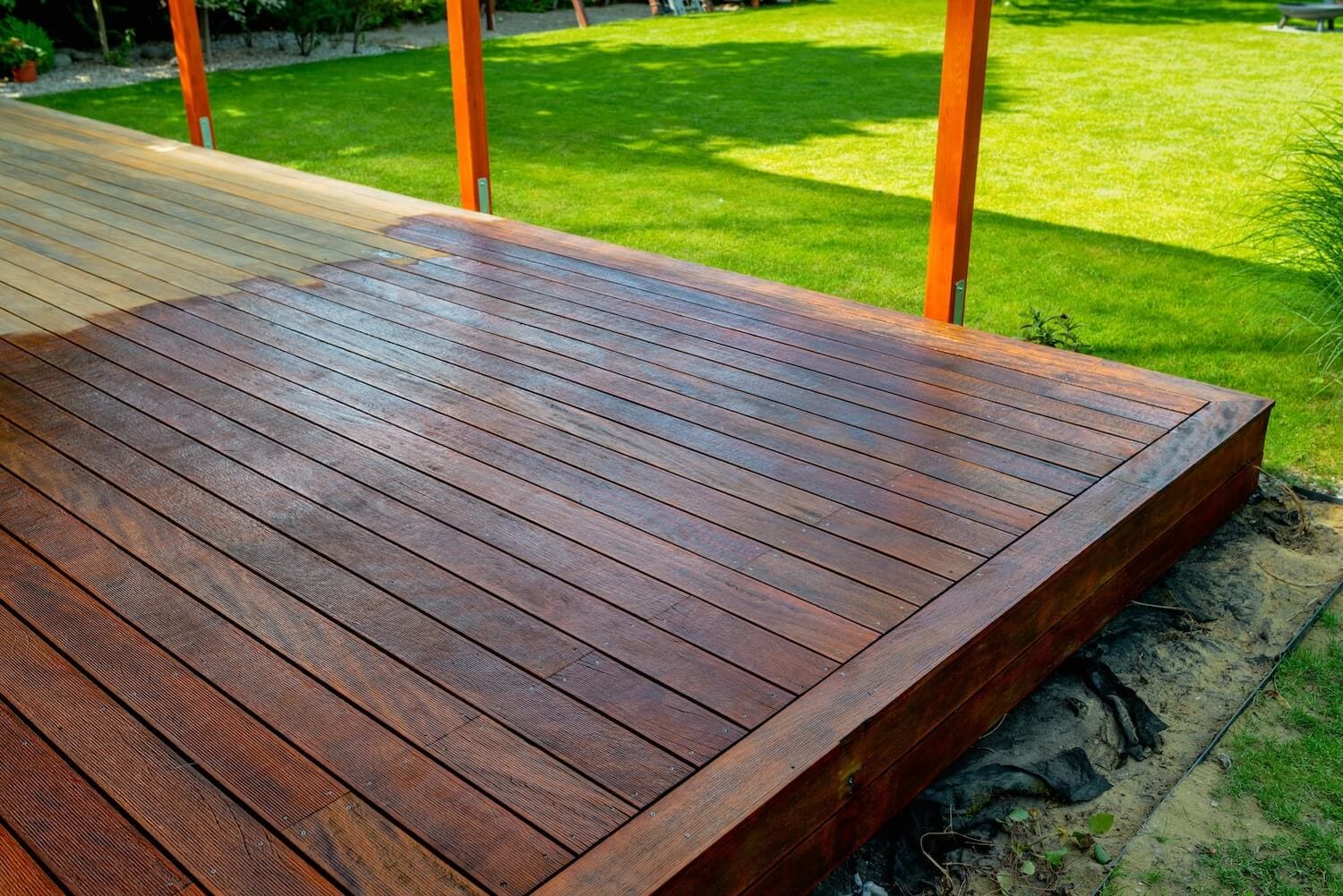 Newly stained hardwood deck with rich brown finish next to a green lawn, deck staining services in Dallas, Texas
