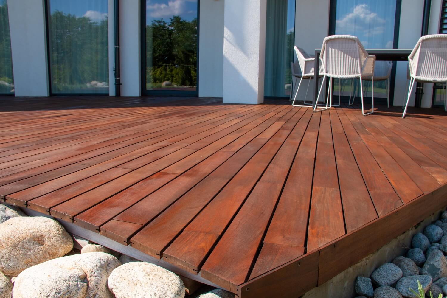 Modern hardwood deck refinished with a deep red stain beside a patio dining set, deck refinishing in Dallas, Texas