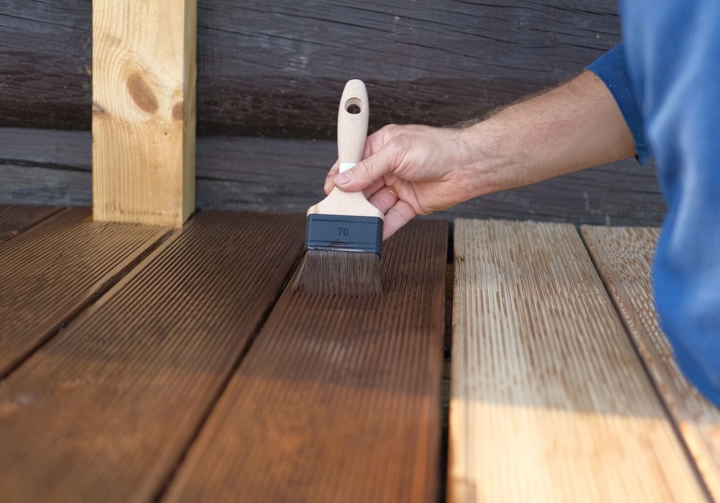 Painter brushing dark stain onto weathered deck boards, showing the before and after of deck staining in Dallas, Texas