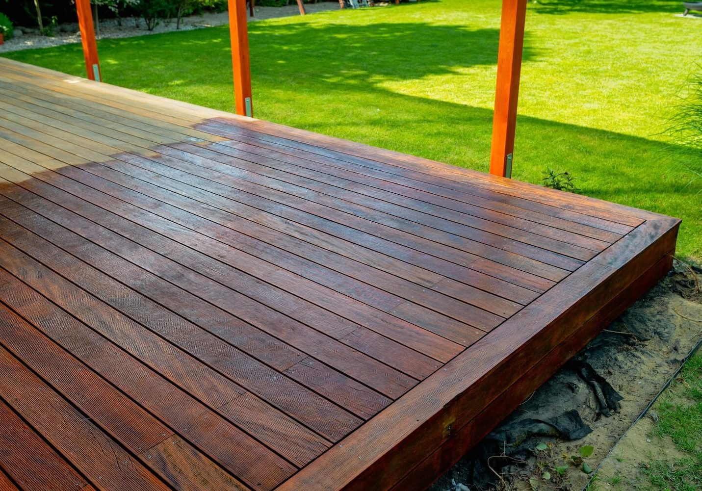 Newly stained hardwood deck with rich brown finish next to a green lawn, deck staining services in Dallas, Texas